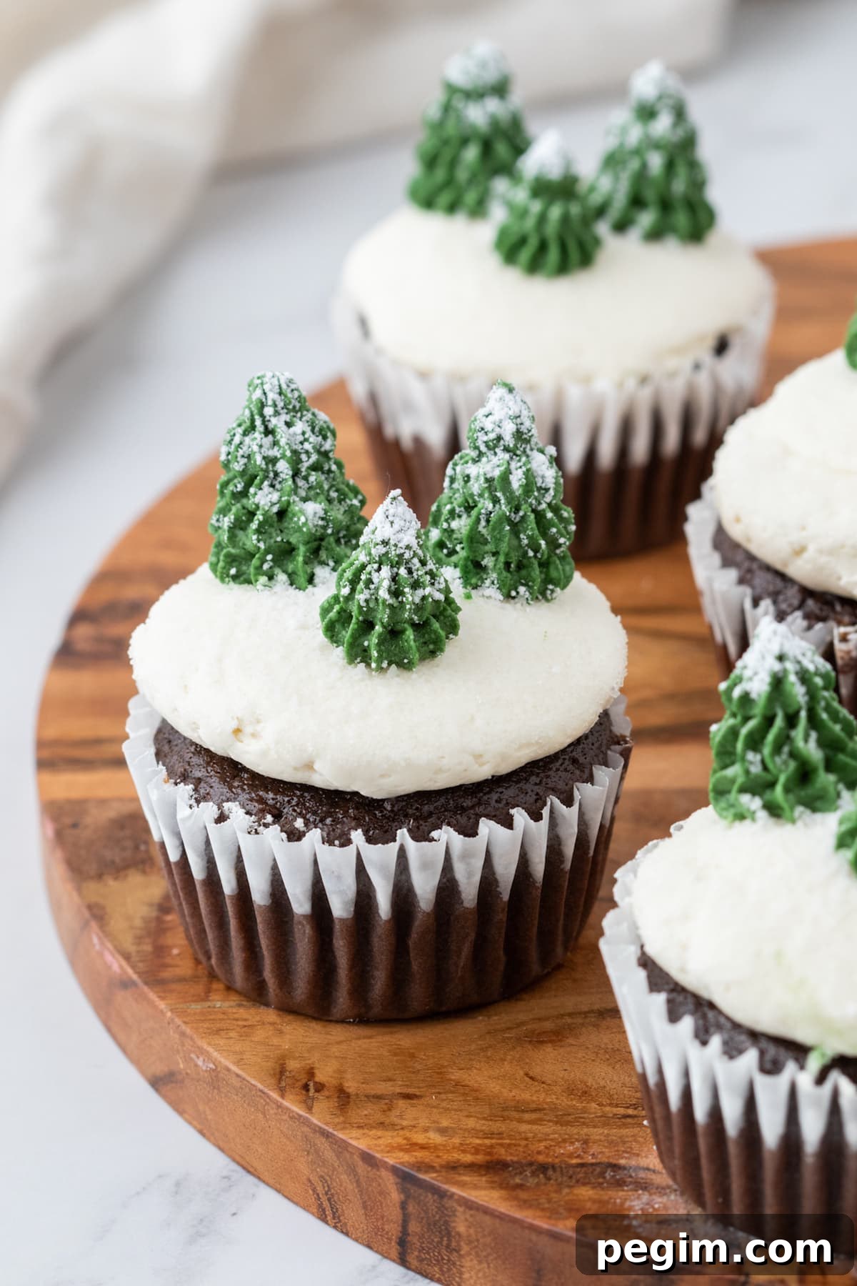 picture of mint chocolate cupcake with buttercream icing, powdered sugar snow, and buttercream piped trees on top on a plate