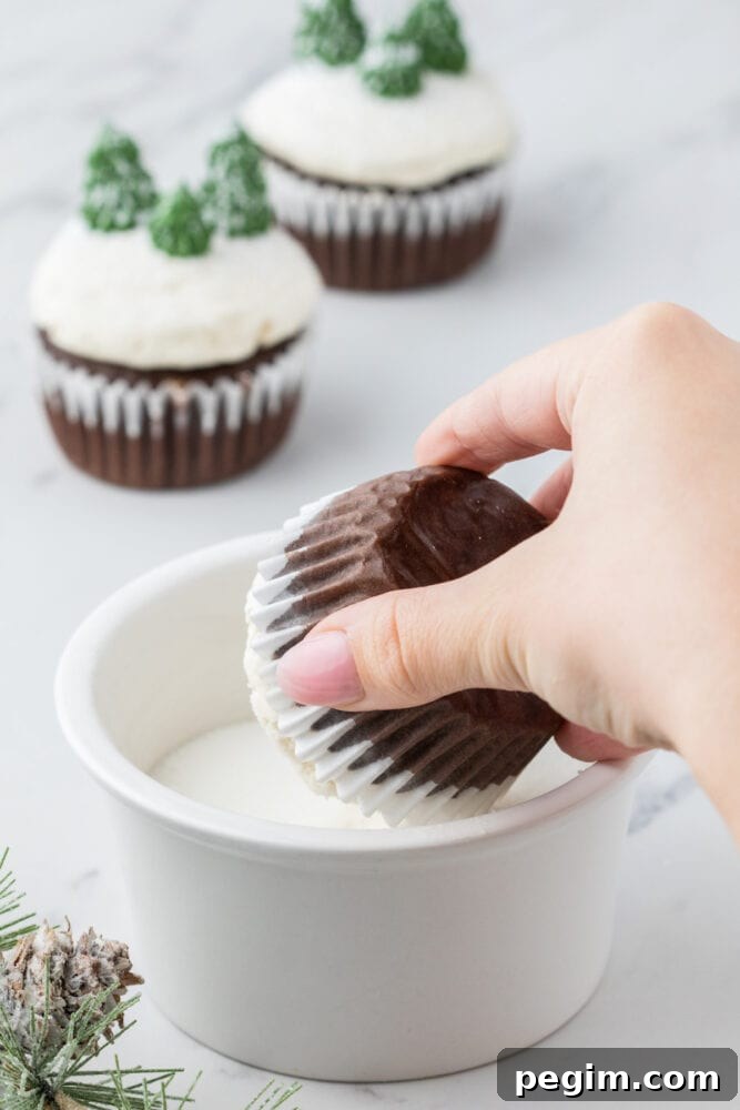 a hand dipping a cupcake in a bowl of powdered sugar