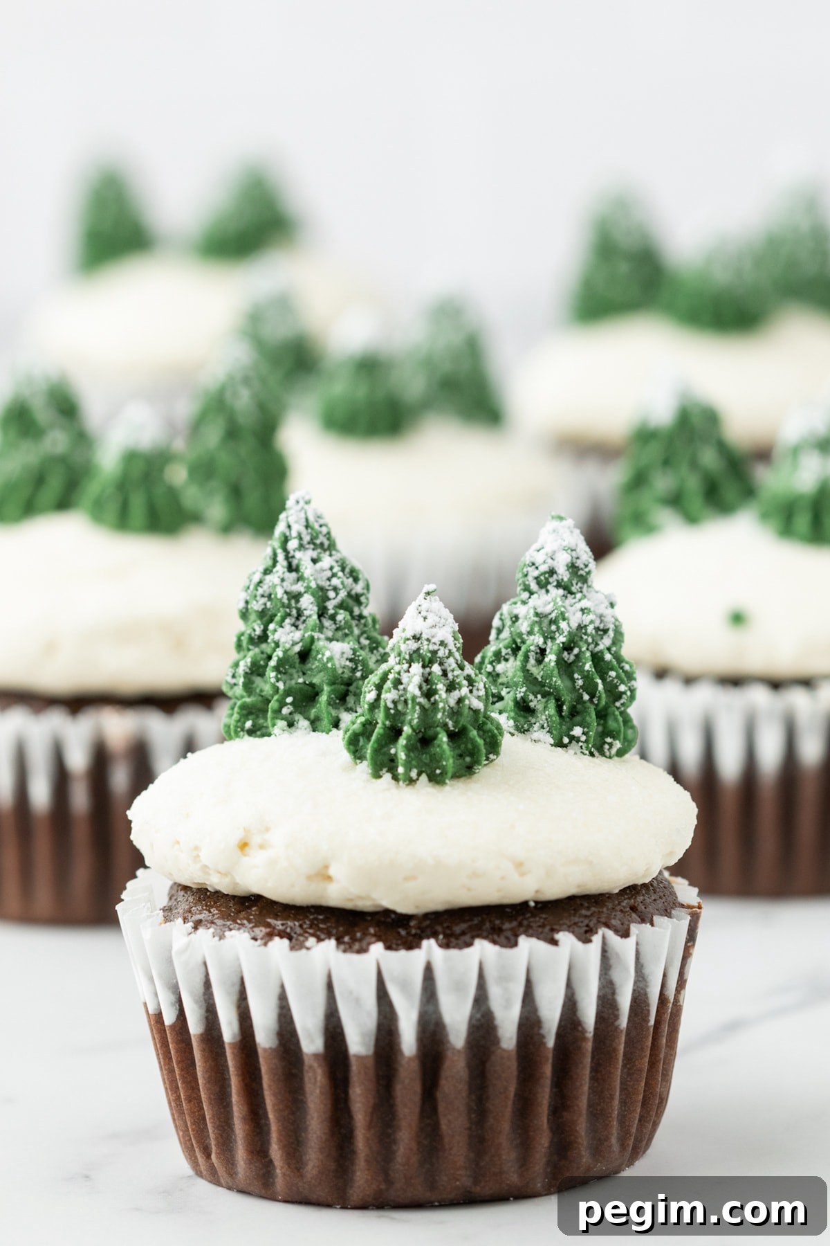 picture of mint chocolate cupcake with buttercream icing, powdered sugar snow, and buttercream piped trees on top on a plate