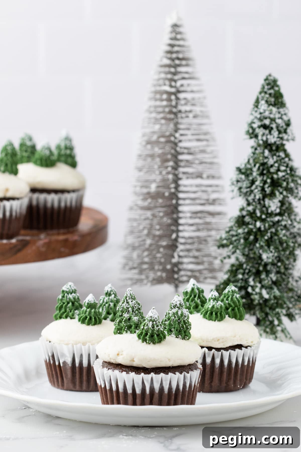 picture of mint chocolate cupcake with buttercream icing, powdered sugar snow, and buttercream piped trees on top on a plate