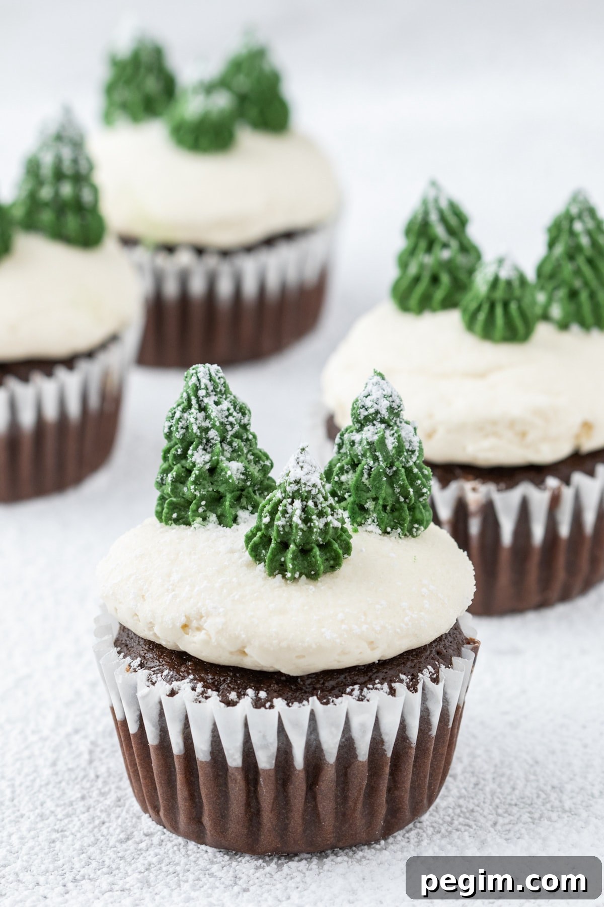 picture of mint chocolate cupcake with buttercream icing, powdered sugar snow, and buttercream piped trees on top on a plate