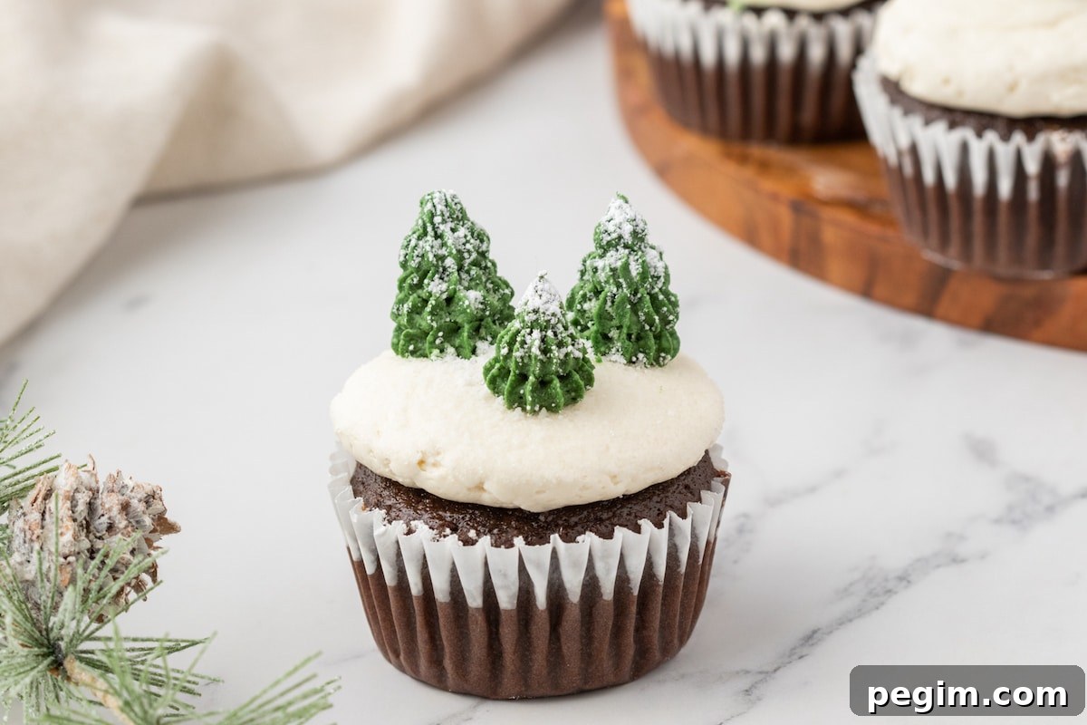 picture of mint chocolate cupcake with buttercream icing, powdered sugar snow, and buttercream piped trees on top on a plate