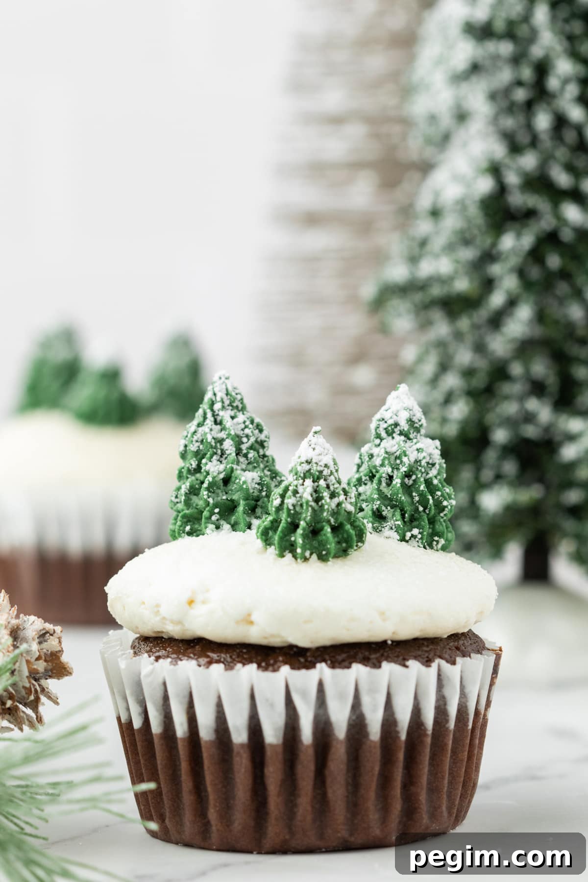 picture of mint chocolate cupcake with buttercream icing, powdered sugar snow, and buttercream piped trees on top on a plate