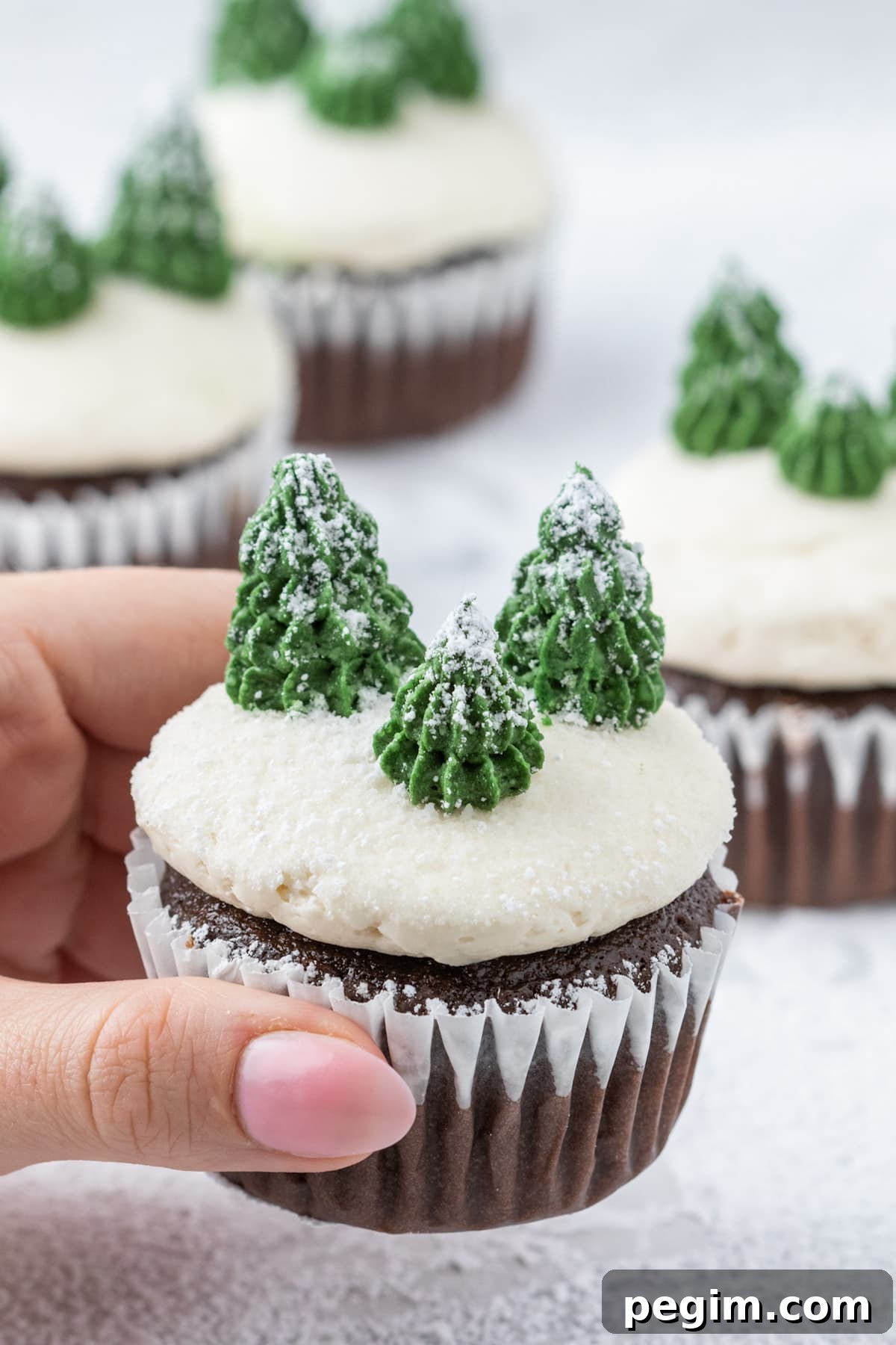 picture of mint chocolate cupcake with buttercream icing, powdered sugar snow, and buttercream piped trees on top on a plate