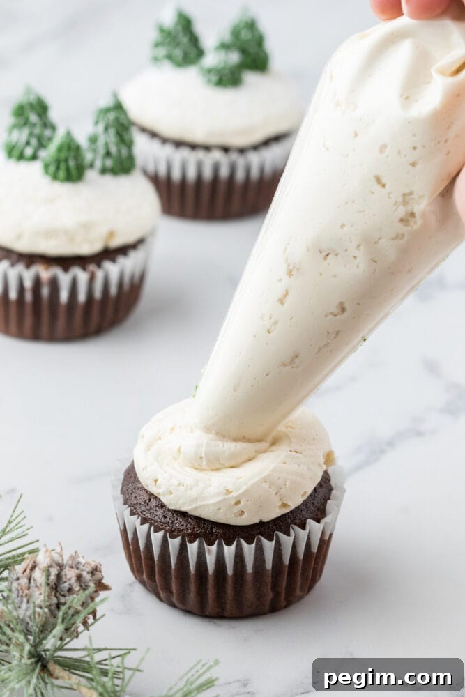 picture of a hand piping white buttercream icing on a chocolate mint cupcake