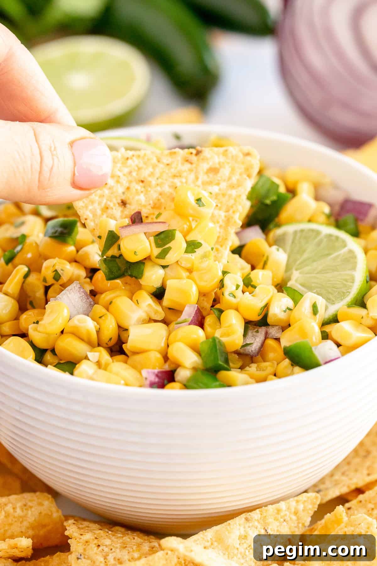 A hand dips a tortilla chip into a bowl of corn salsa.