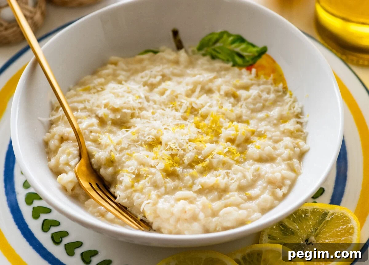 A bowl of lemon risotto with a fork resting in it and lemon slices lined on the edge of the plate.