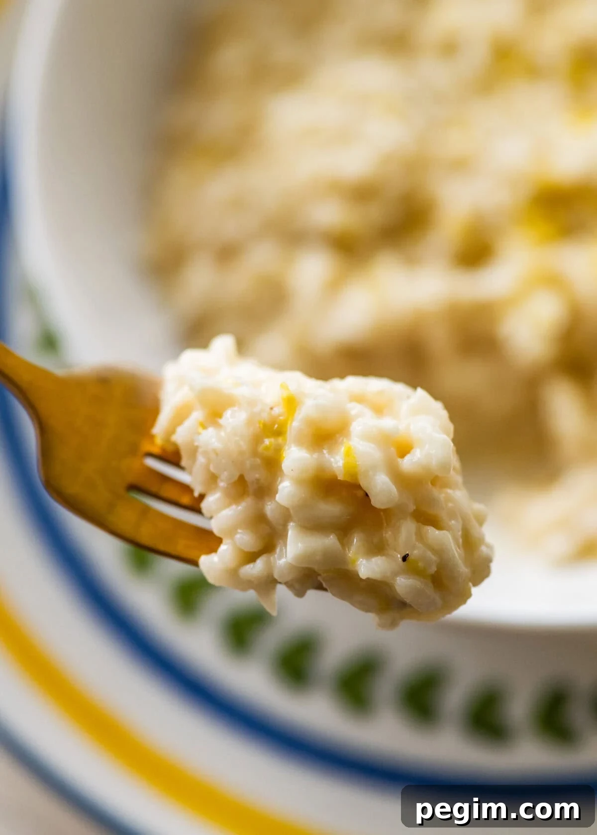 One bite of lemon risotto on a fork held over a bowl of more risotto.
