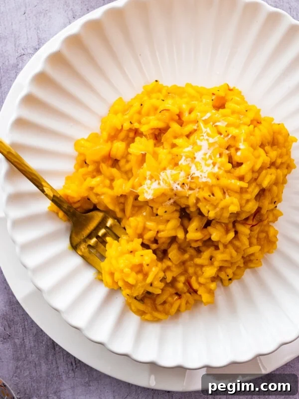 Risotto alla Milanese on a white plate with parmigiano on top.