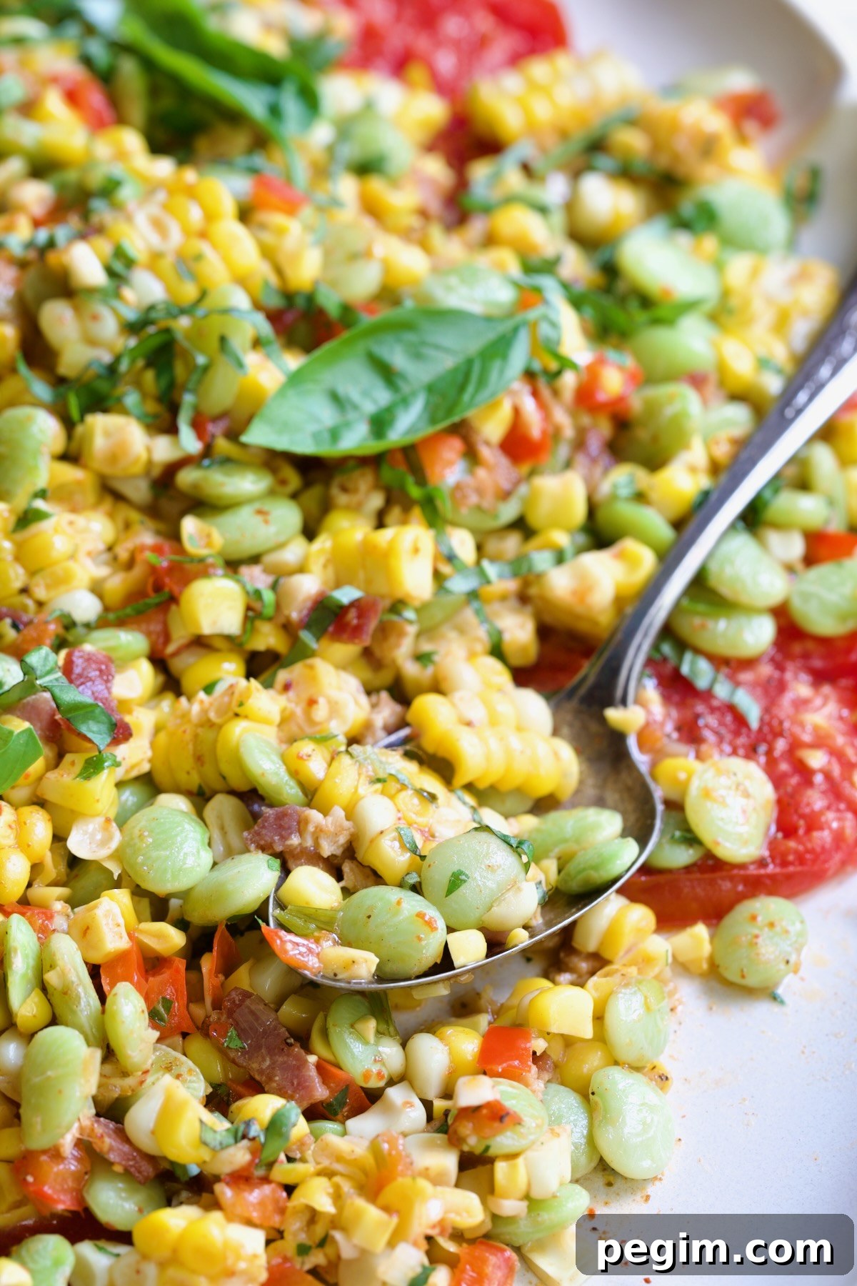 Grilled Corn Succotash garnished with fresh basil on white oval platter with serving spoon scooping some up.