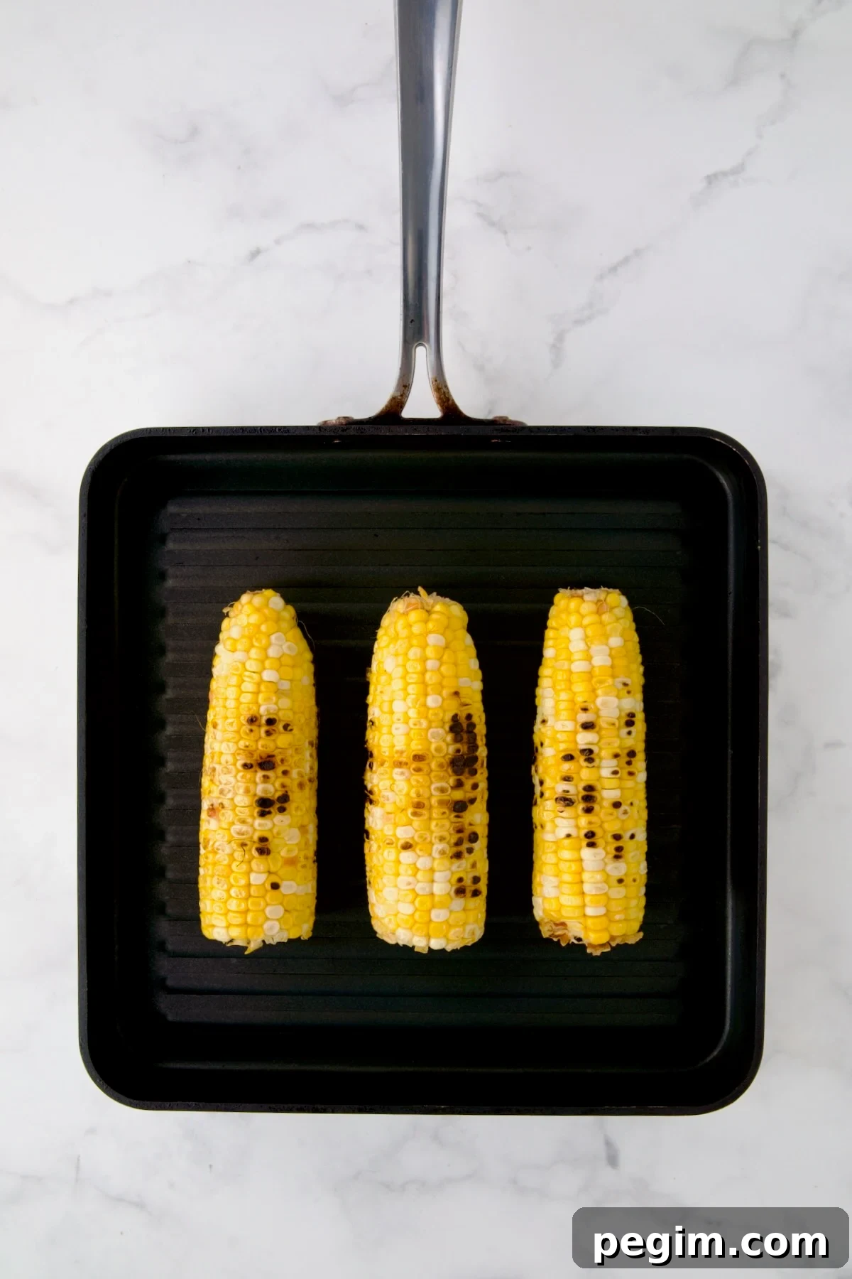 Three ears of corn being grilled on grill pan.