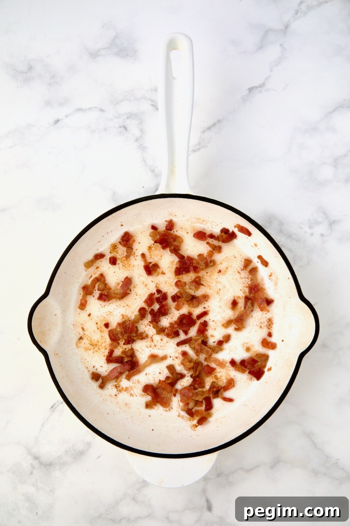 Bacon being crisped in white enamel cast iron skillet.