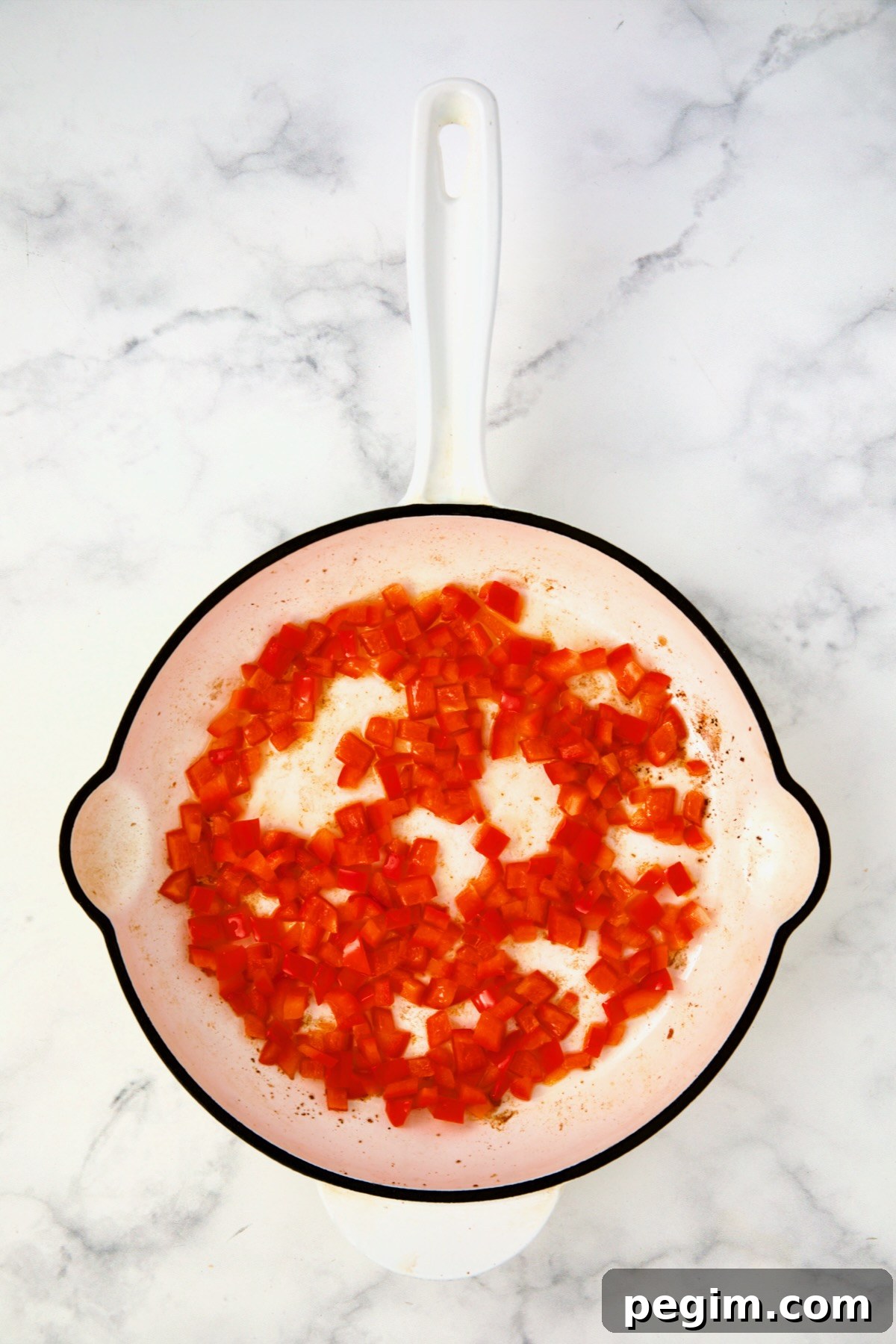 Cooked red bell pepper in white enamel cast iron skillet.