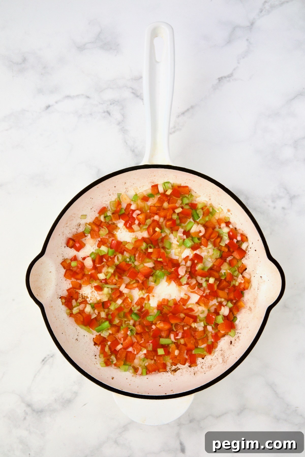 Cooked red bell pepper and scallion in white enamel cast iron skillet.
