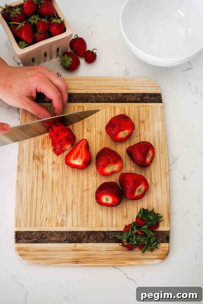 A knife dices strawberries on a wooden cutting board.