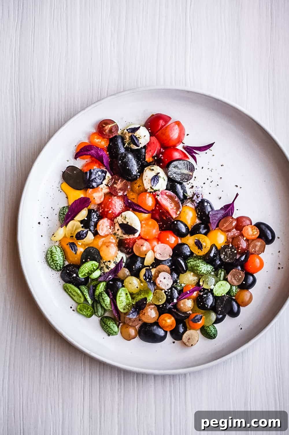a summer salad with cherry tomatoes, cucuamelons, grapes, basil and cheese arranged on a plate.