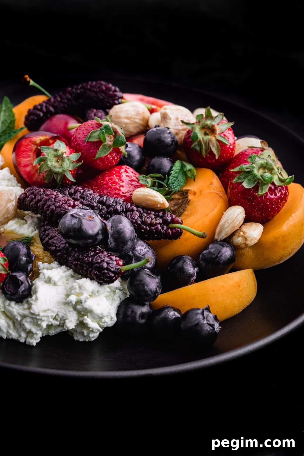 Single angle shot of Summer fruit with fresh cheese, almonds and honey on a black plate and background.