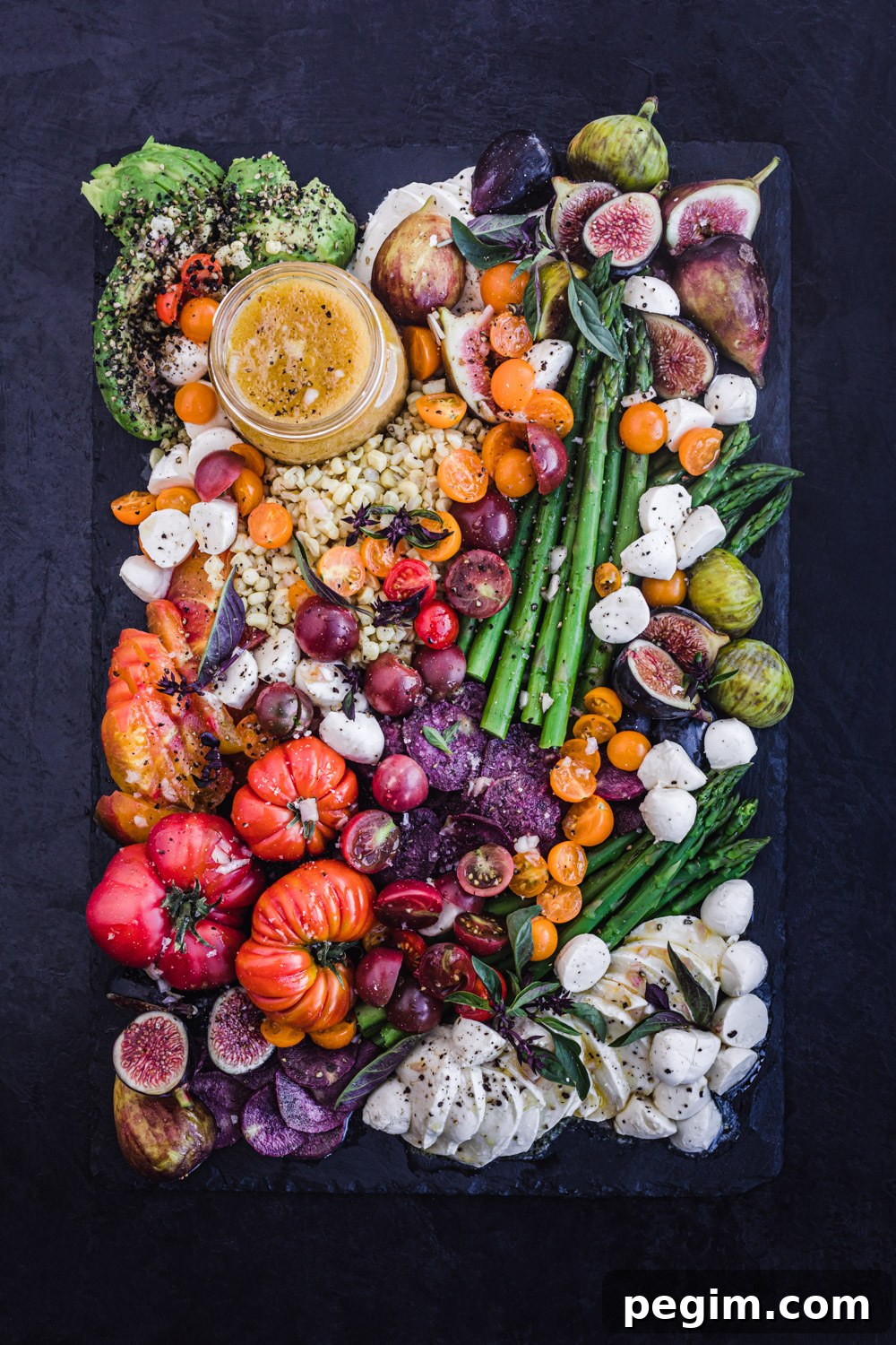Summer salad board filled with seasonal summer fruit and veggies, overhead shot on a black background.
