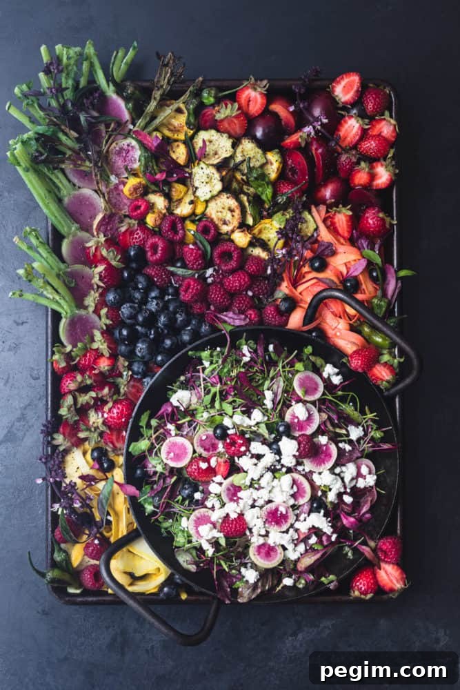 summer farmers market bounty made into a salad board! summer fruits, veggies, greens and cheese arranged on a tray on a black background.