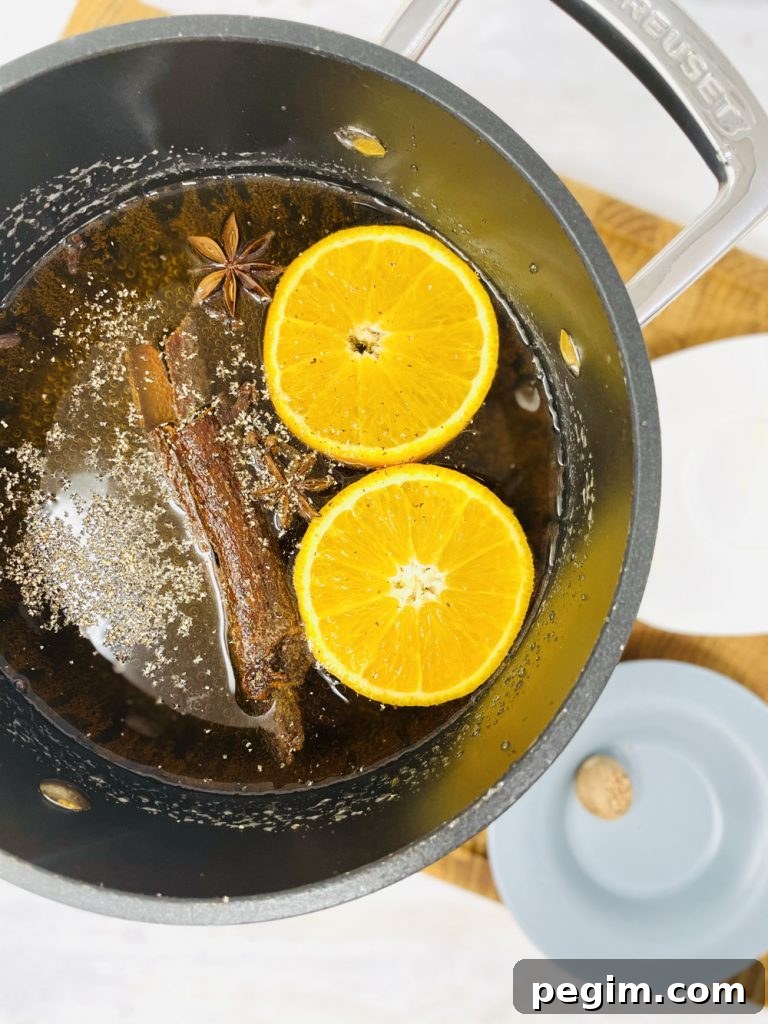 mulled cider in a saucepan with mulled cider spices and orange slices