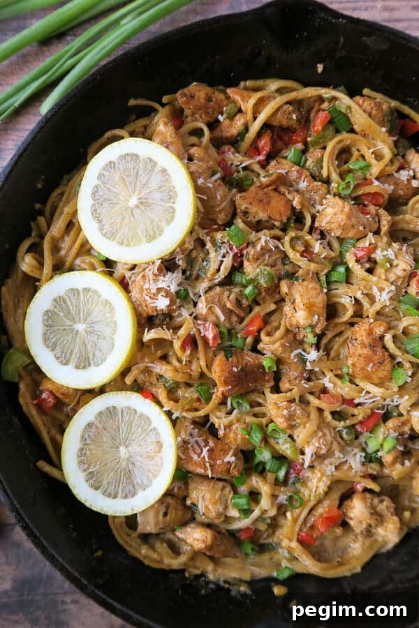 creamy cajun chicken pasta garnished with lemon wedges, grated parmesan cheese, and green onions.