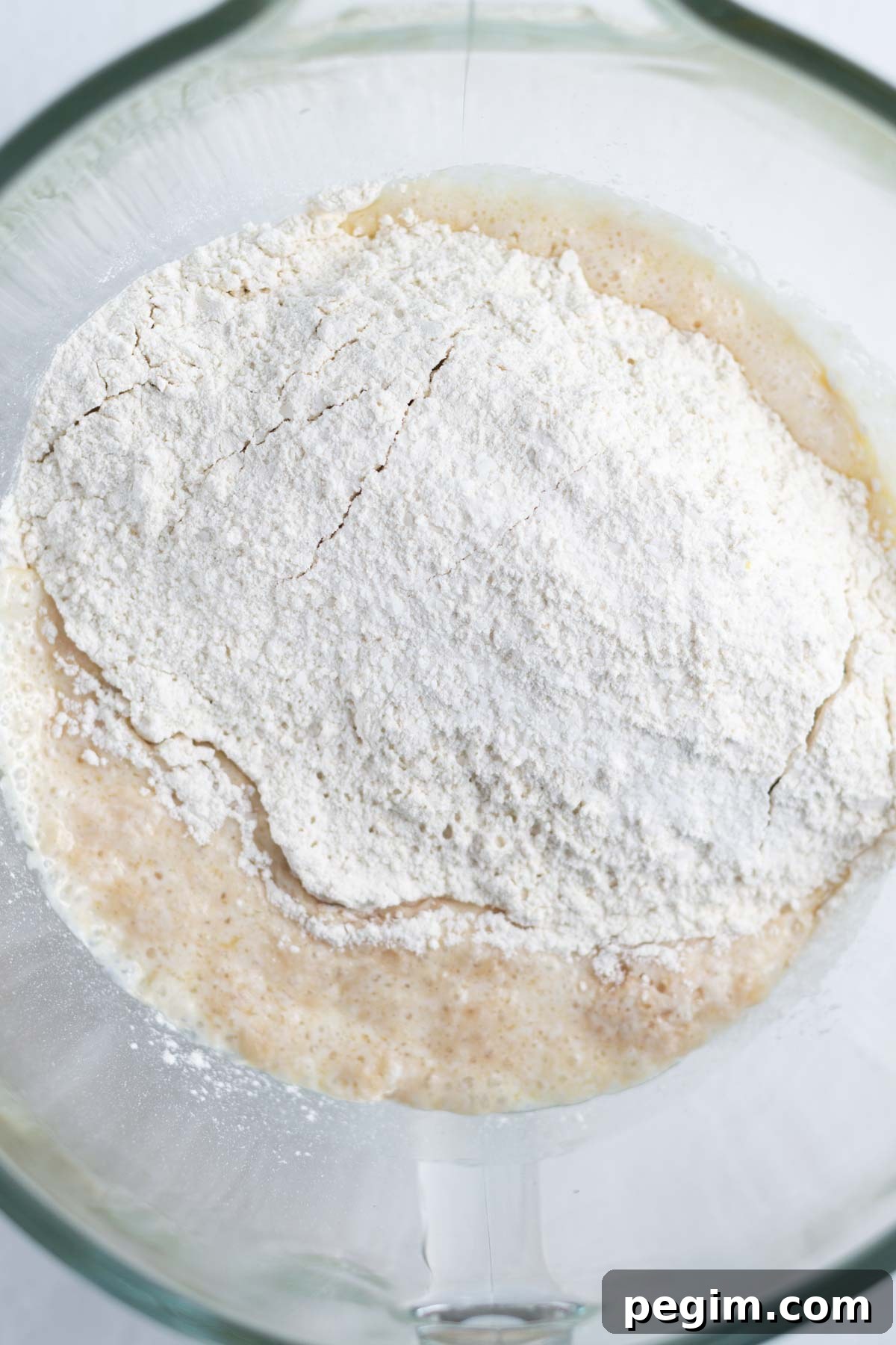 flour added on top of activated yeast, sugar and melted butter in a mixing bowl