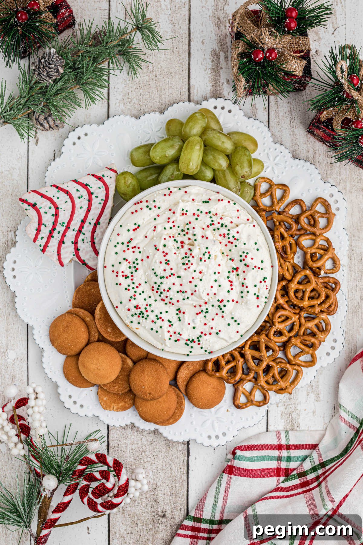 Overhead shot of a plate, with a bowl of Christmas Tree Dip, surrounded by cookies and fruit to dip into.