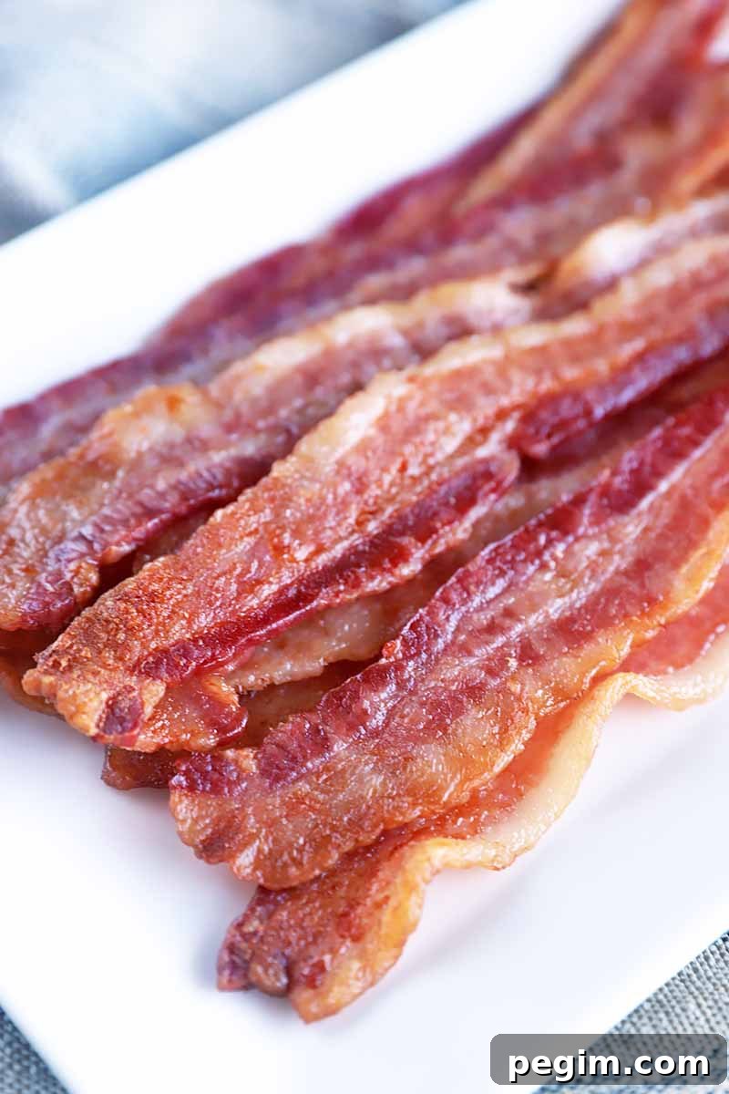 Vertical image of a rectangular white plate with cooked strips of breakfast meat.