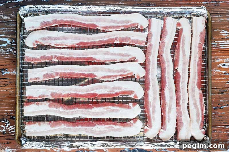Horizontal image of slices of uncooked meat on a cooling rack over a baking sheet lined with aluminum foil.