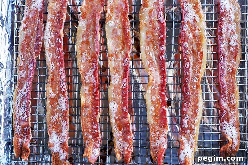 Horizontal image of cooked slices of meat on a cooling rack lined with aluminum foil to catch the dripping fat.