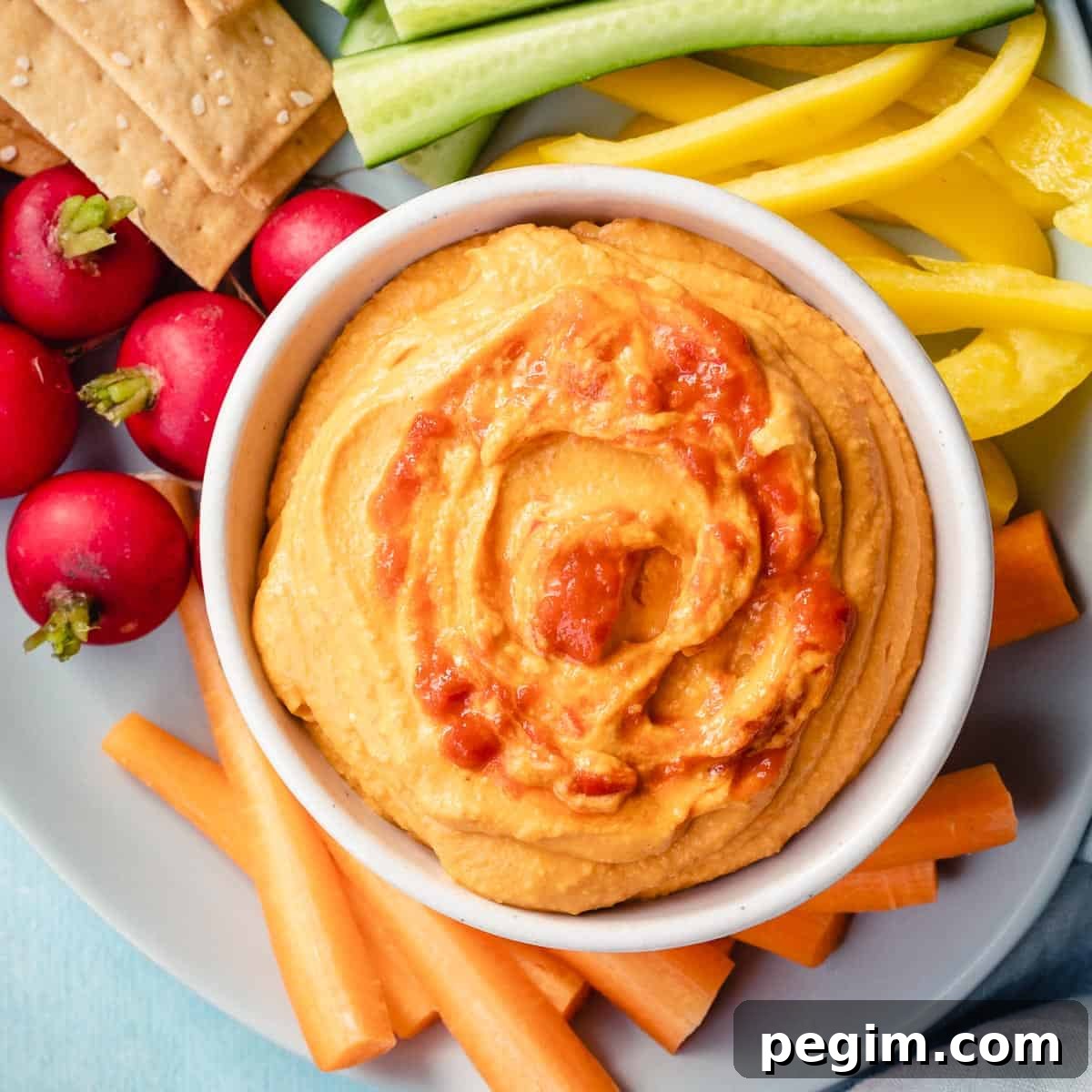 close up of harissa hummus in small bowl next to radishes, carrot sticks, and peppers.