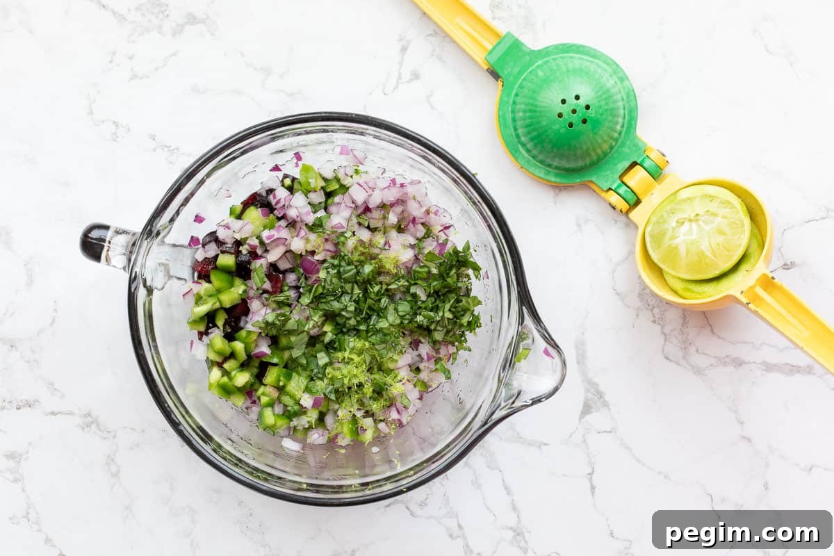 mixing bowl with chopped cherries, peppers, red onions, basil, lime zest next to lemon squeezer with lime halves.