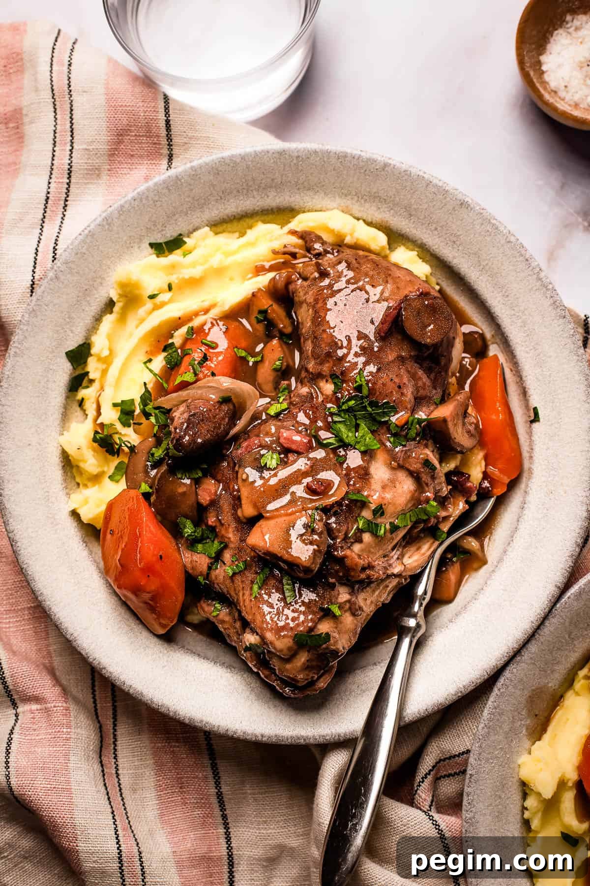 A serving of coq au vin with mashed potatoes on a stoneware plate.