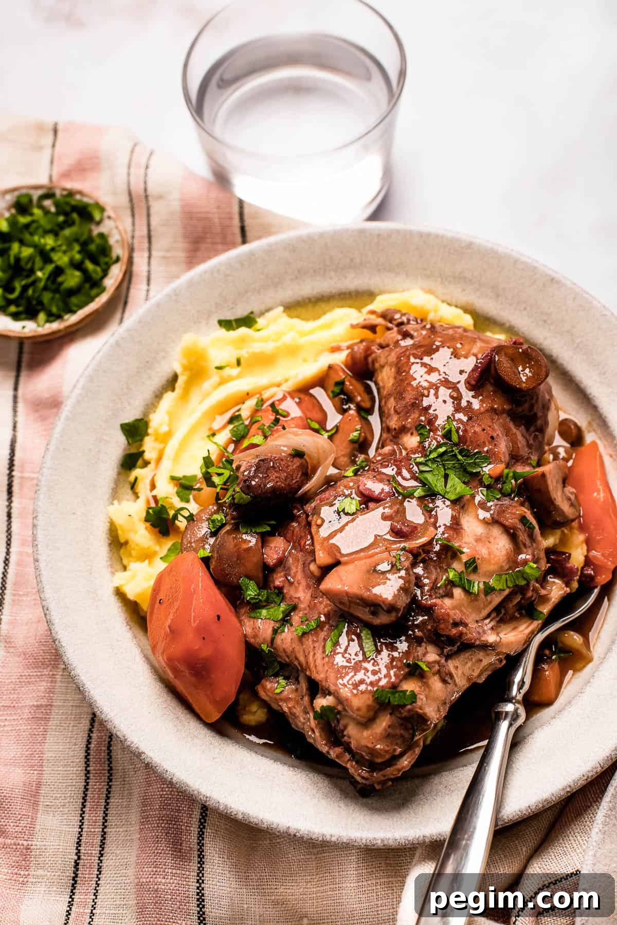 A serving of coq au vin with mashed potatoes on a stoneware plate.