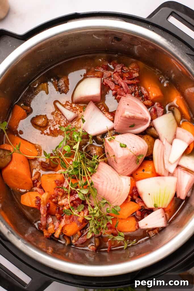 Overhead shot of onions, chicken thyme, and carrots in red wine sauce.