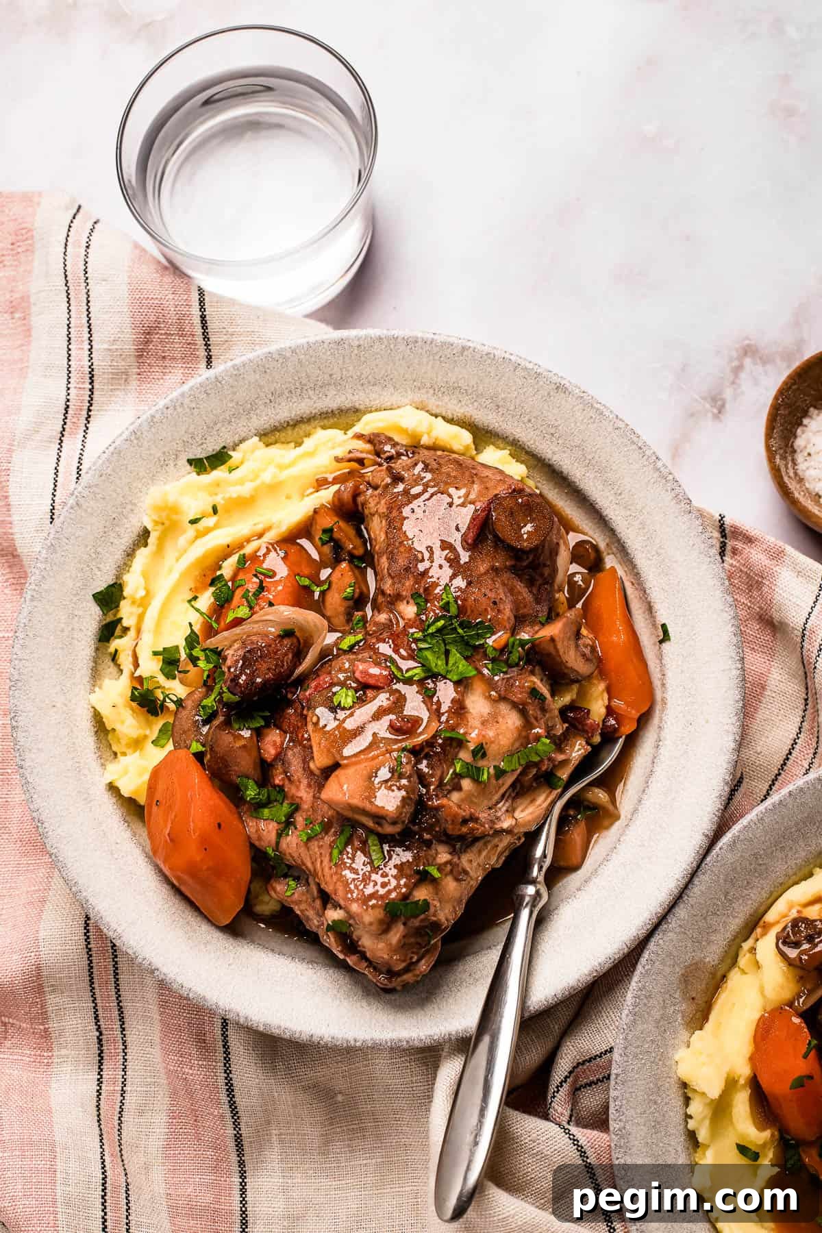 A serving of coq au vin with mashed potatoes on a stoneware plate.