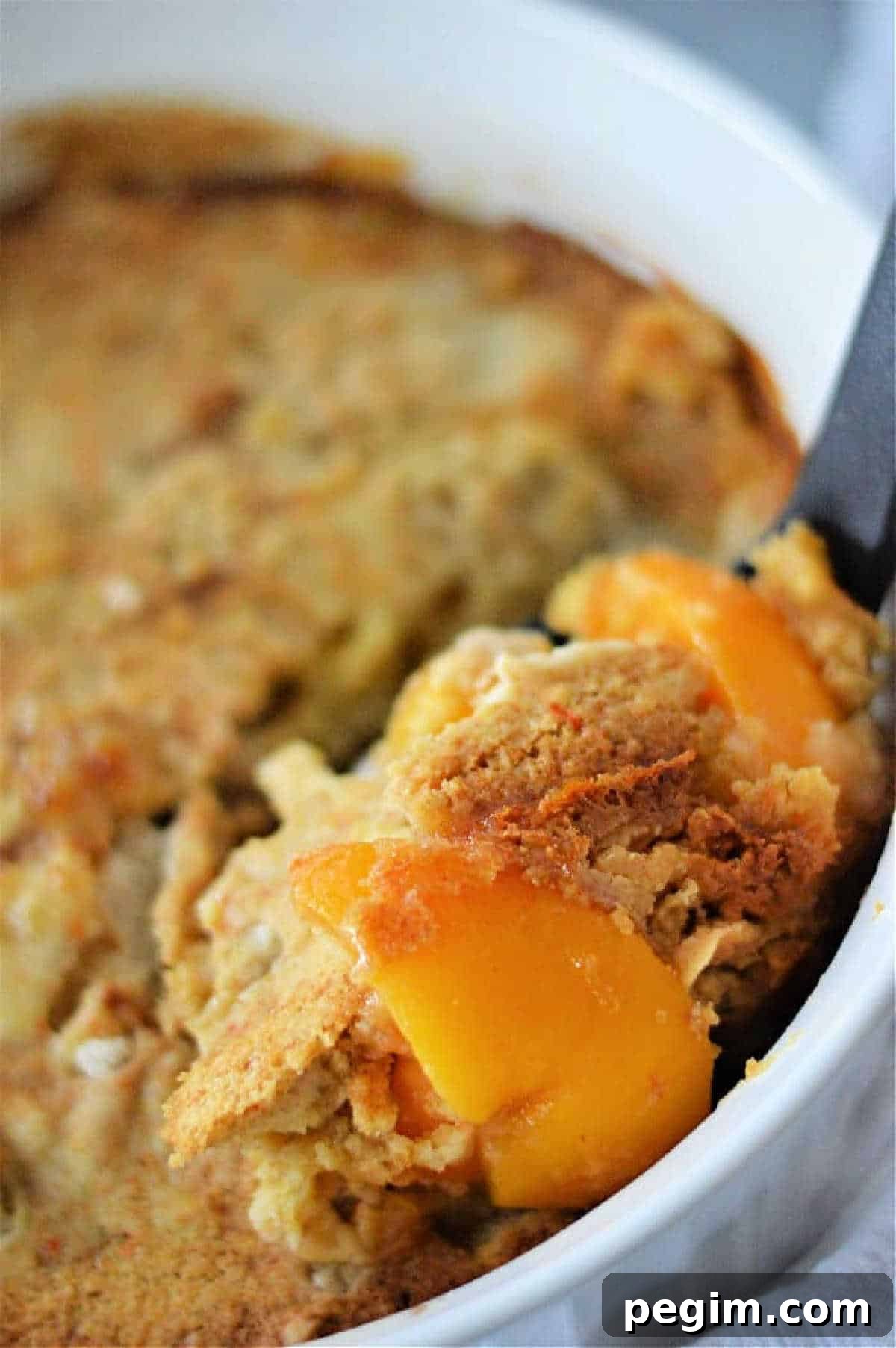 Old-Fashioned Peach Cobbler Made with Cake Mix 5 A close-up of a serving of peach cobbler with cake mix being scooped from a white baking dish.