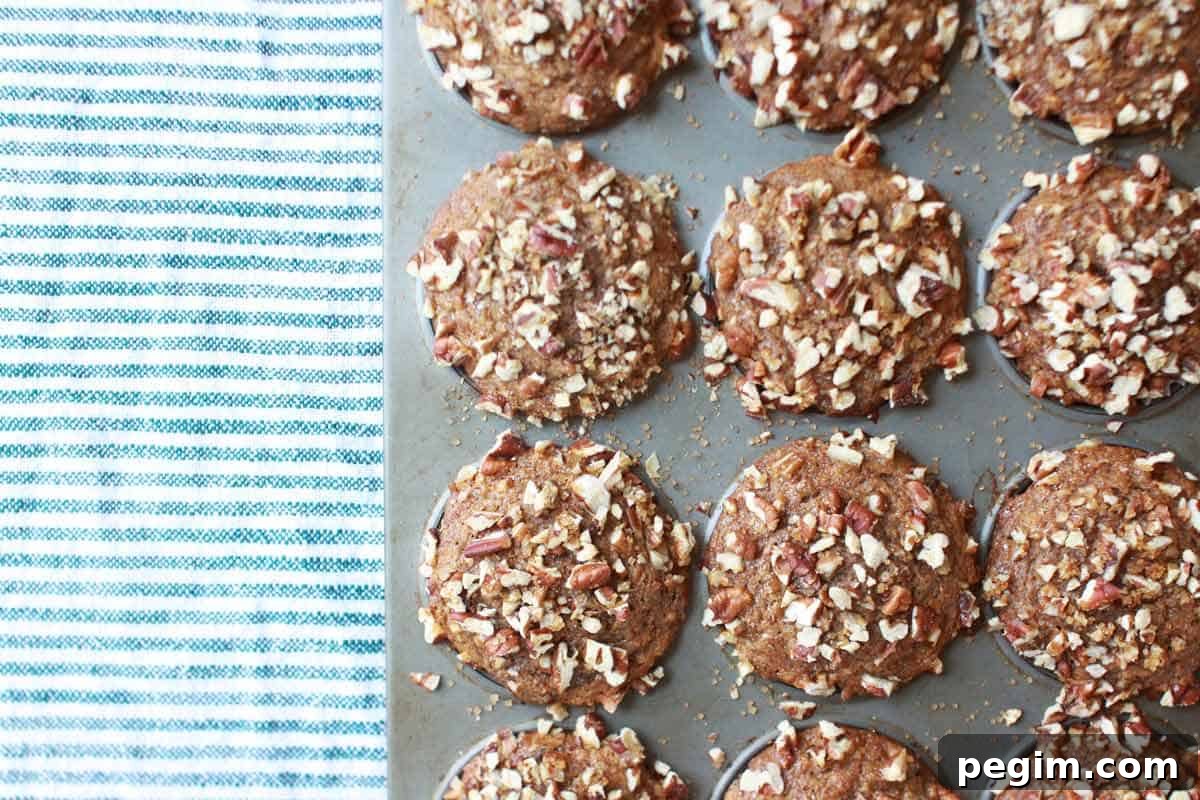 Whole Wheat Banana Nut Muffins Recipe 3 a muffin pan with freshly baked banana nut muffins in it and a striped tea towel laying next to it