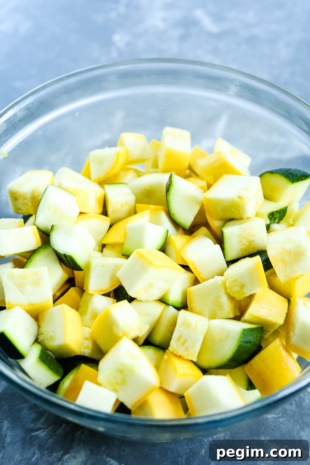 Crispy Air Fryer Zucchini and Yellow Squash in 15 Minutes 5 zucchini and squash cut into triangle shapes pieces in a clear glass bowl
