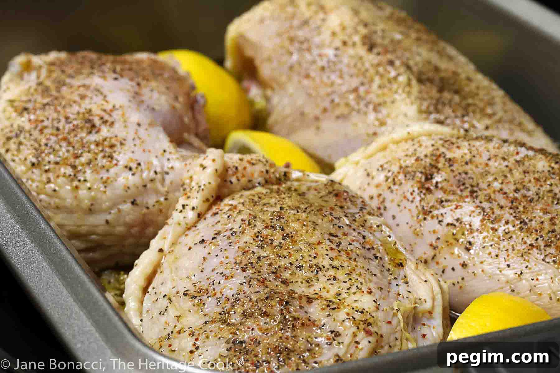 Chicken breasts seasoned and ready for the oven with lemon wedges tucked between them. 