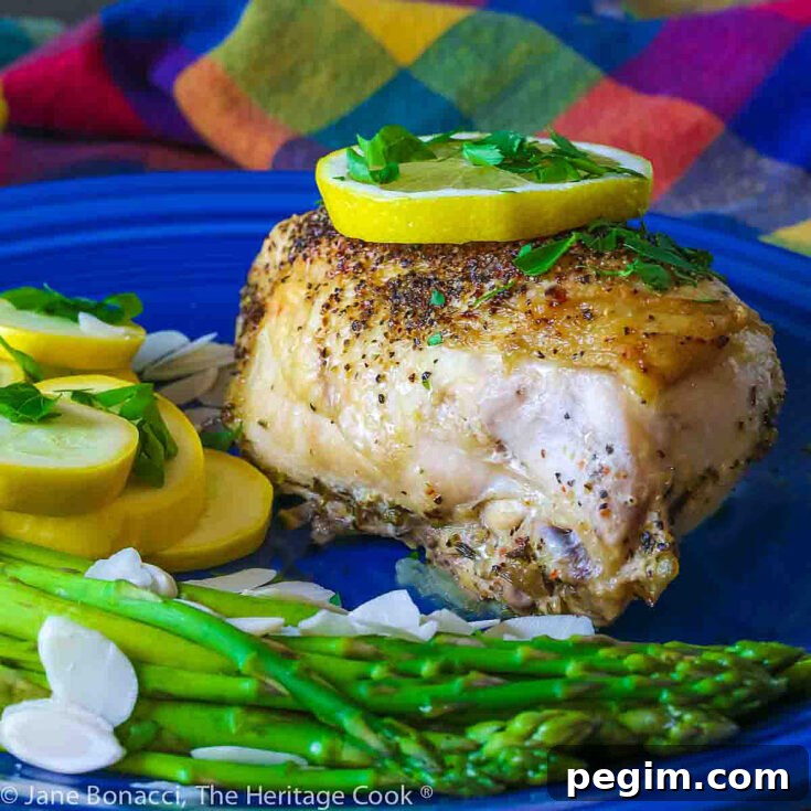 Large baked lemon chicken breast with a slice of lemon on top and green asparagus next to yellow squash on a blue plate © 2024 Jane Bonacci, The Heritage Cook.