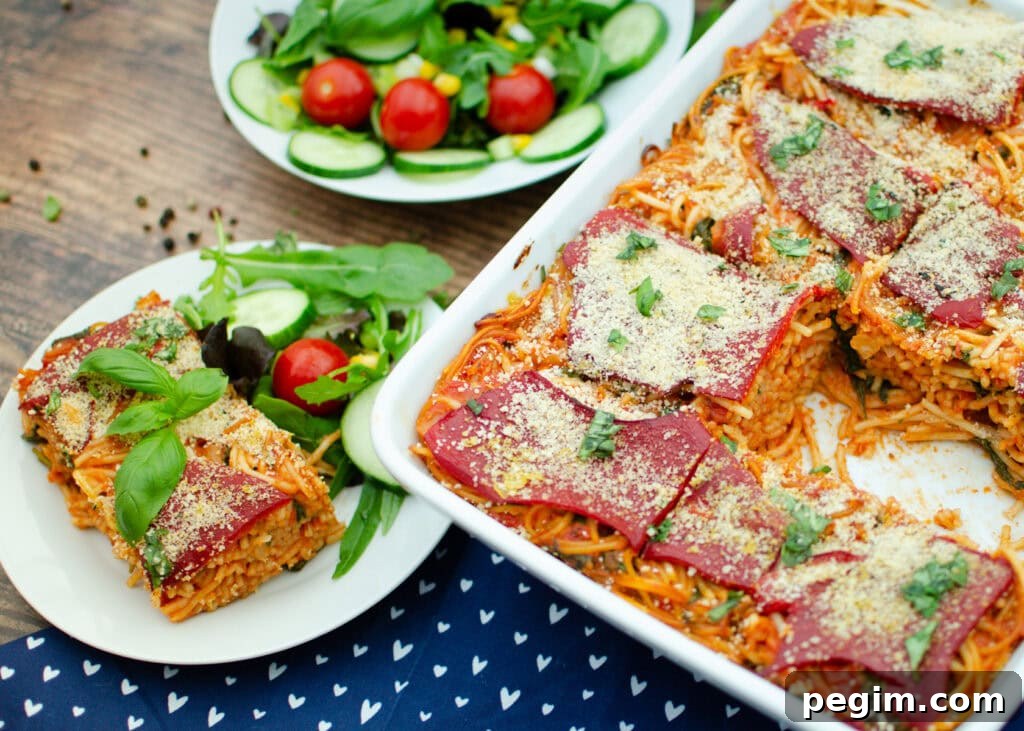 Sun-Dried Tomato & Roasted Pepper Pasta Recipe for Quick Weeknights 6 spicy vegan pasta bake served in a white casserole dish on a blue and white towel and the pasta served on a white plate with salad on the side