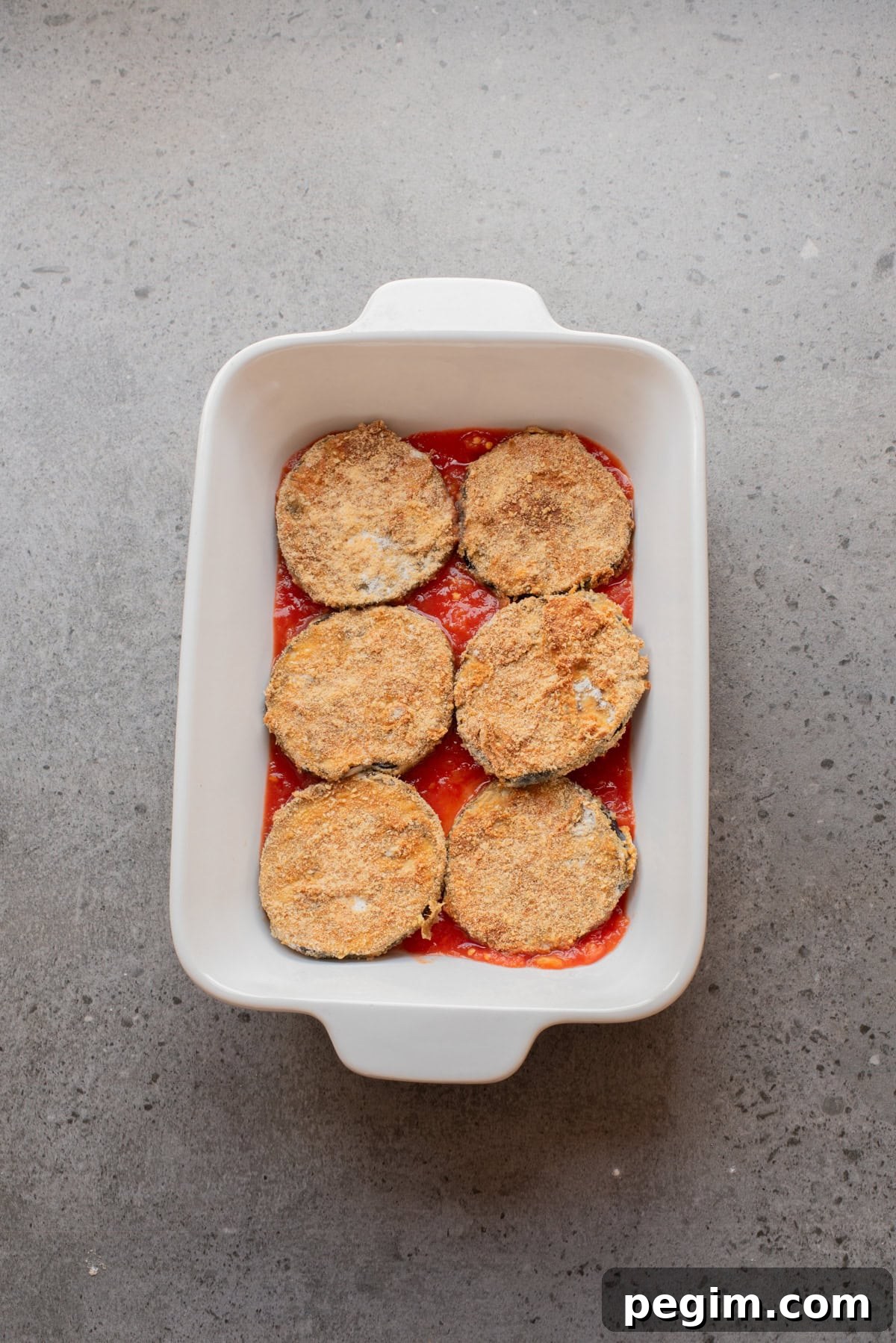 Crispy Baked Eggplant Parmesan Recipe 8 An overhead image is layering eggplant slices, marinara sauce, and cheese in a baking sheet.