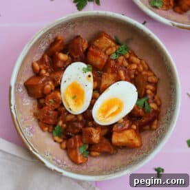 A bowl of chicken sausage pieces, beans and potatoes with a boiled egg on top.
