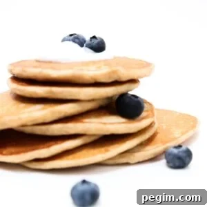Protein-Packed Pancakes Without Protein Powder: High-Protein Recipe 9 A stack of protein pancakes topped with a small amount of yogurt and a few blueberries.