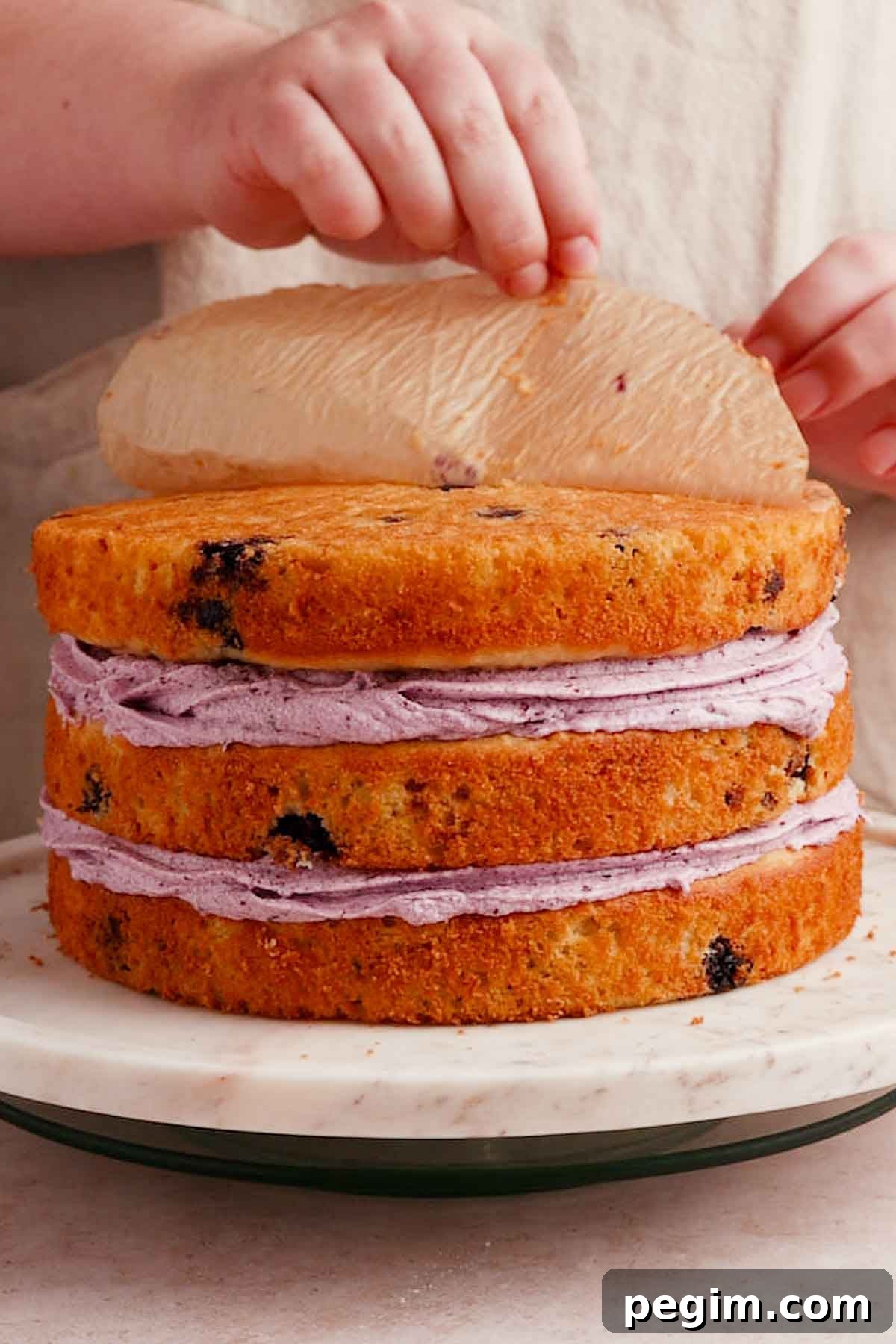 Blueberry Birthday Cake Recipe — Moist Layer Cake for Parties 15 stacked cake layers with filling and peeling off the parchment paper off the bottom of the top layer