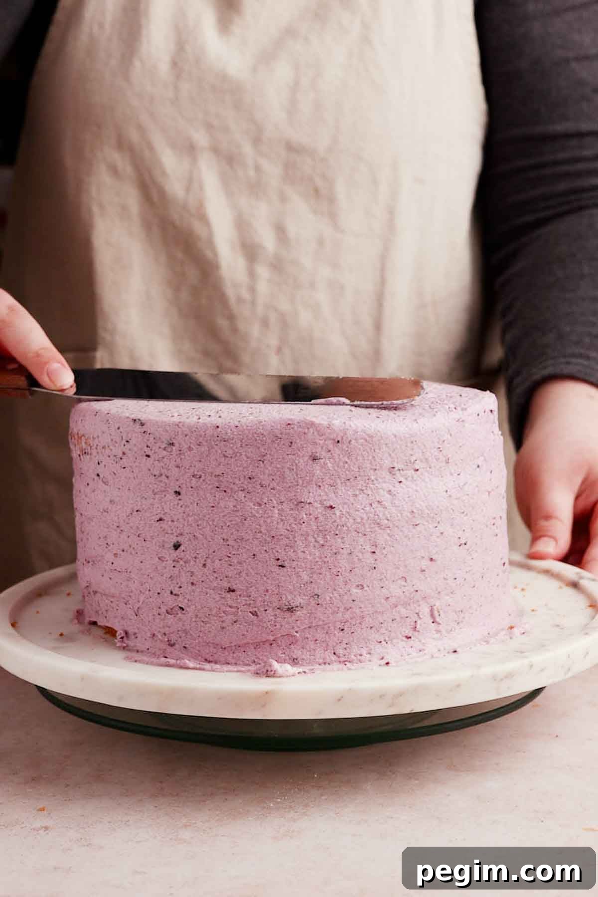 Blueberry Birthday Cake Recipe — Moist Layer Cake for Parties 16 smoothing frosting on blueberry birthday cake with a long metal spatula