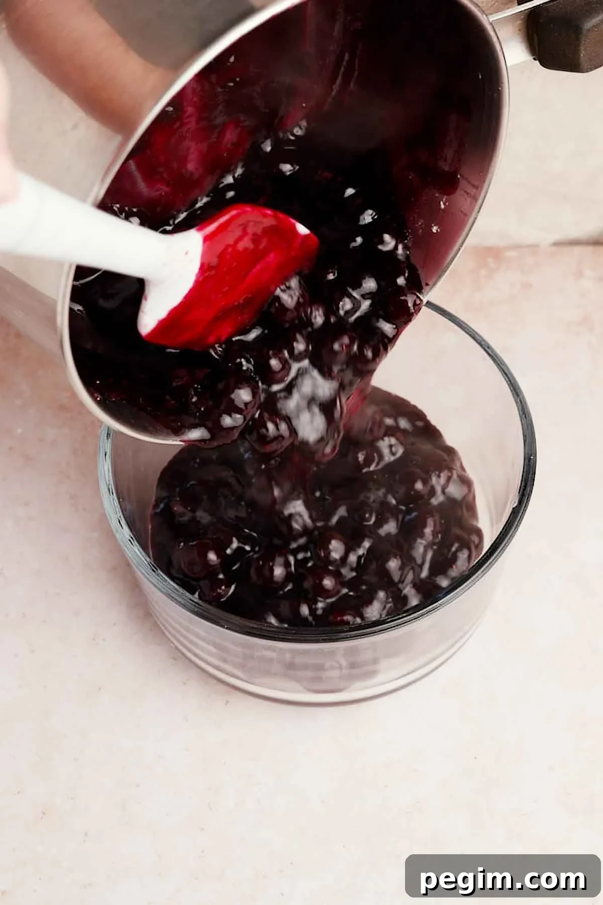 Blueberry Birthday Cake Recipe — Moist Layer Cake for Parties 10 pouring blueberry filling from a saucepan into a glass container
