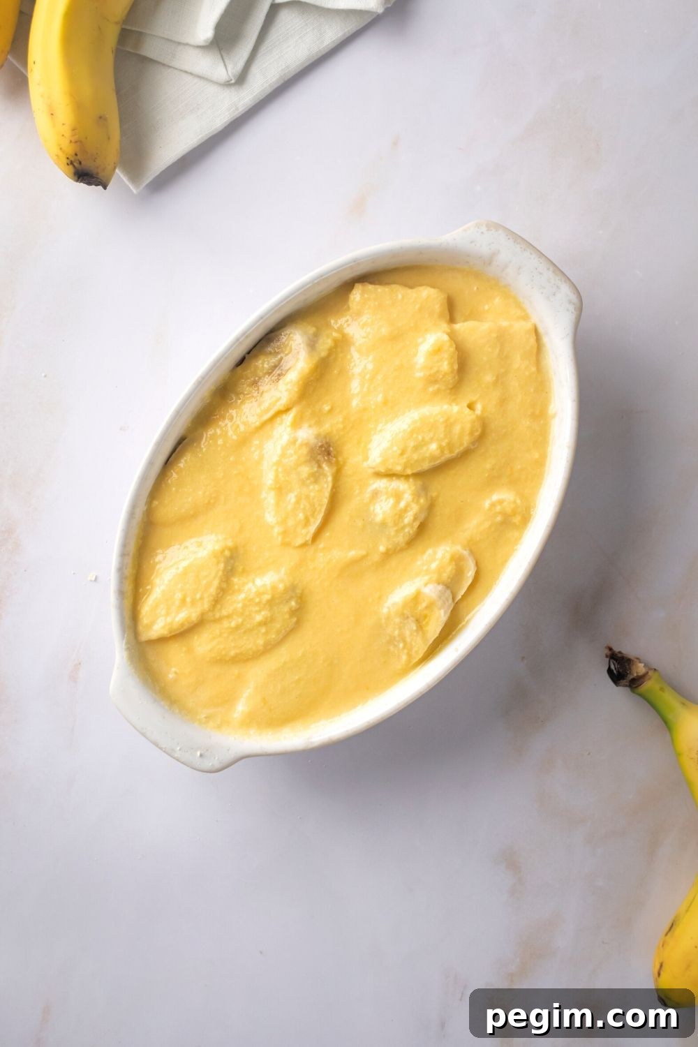 A pudding mixture covering bananas in a white casserole dish.
