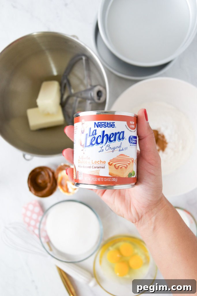 Cinnamon Churro Cake with Crispy Sugar Crust 4 A hand holds a can of La Lechera dulce de leche above cake ingredients in bowls